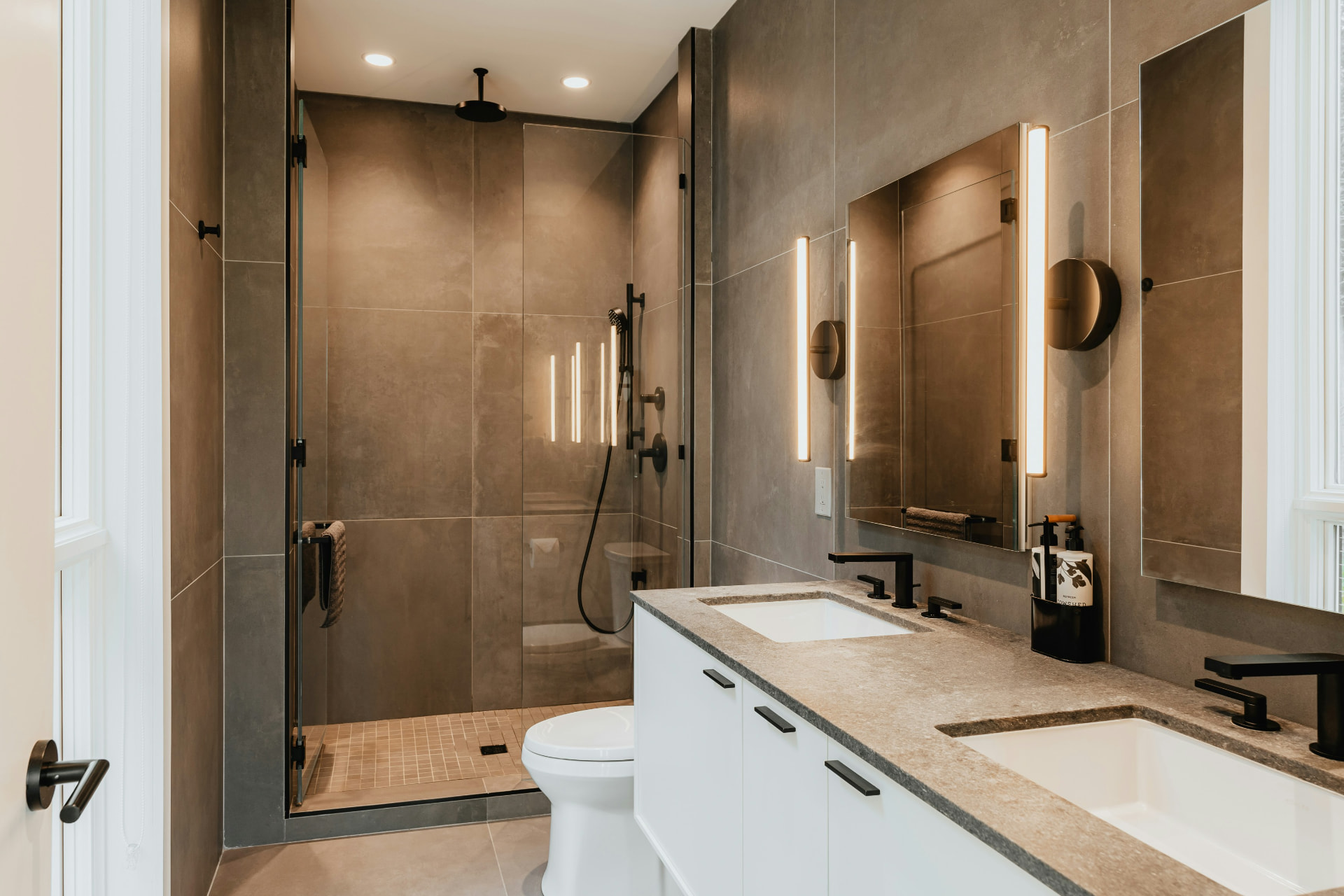 Modern bathroom with large-format stone tile, backlit mirrors and a double stone-top vanity